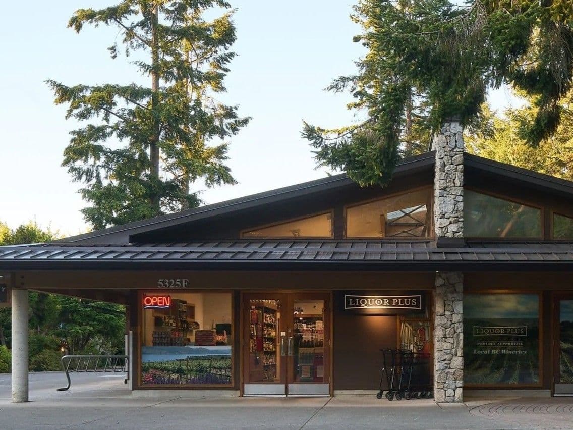Liquor Plus storefront at golden hour, framed by tall evergreens