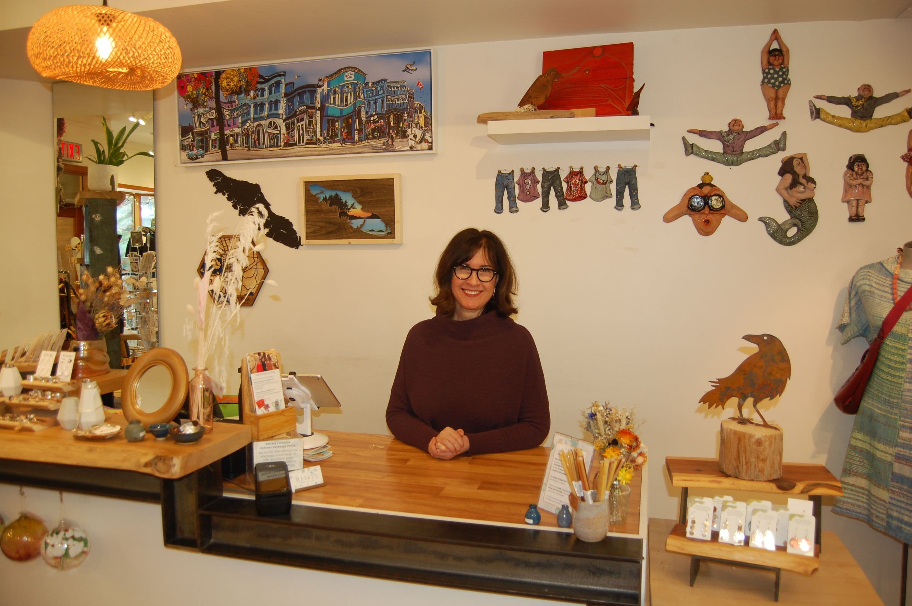 Shopkeeper smiling behind the counter beneath local art and a raven sculpture