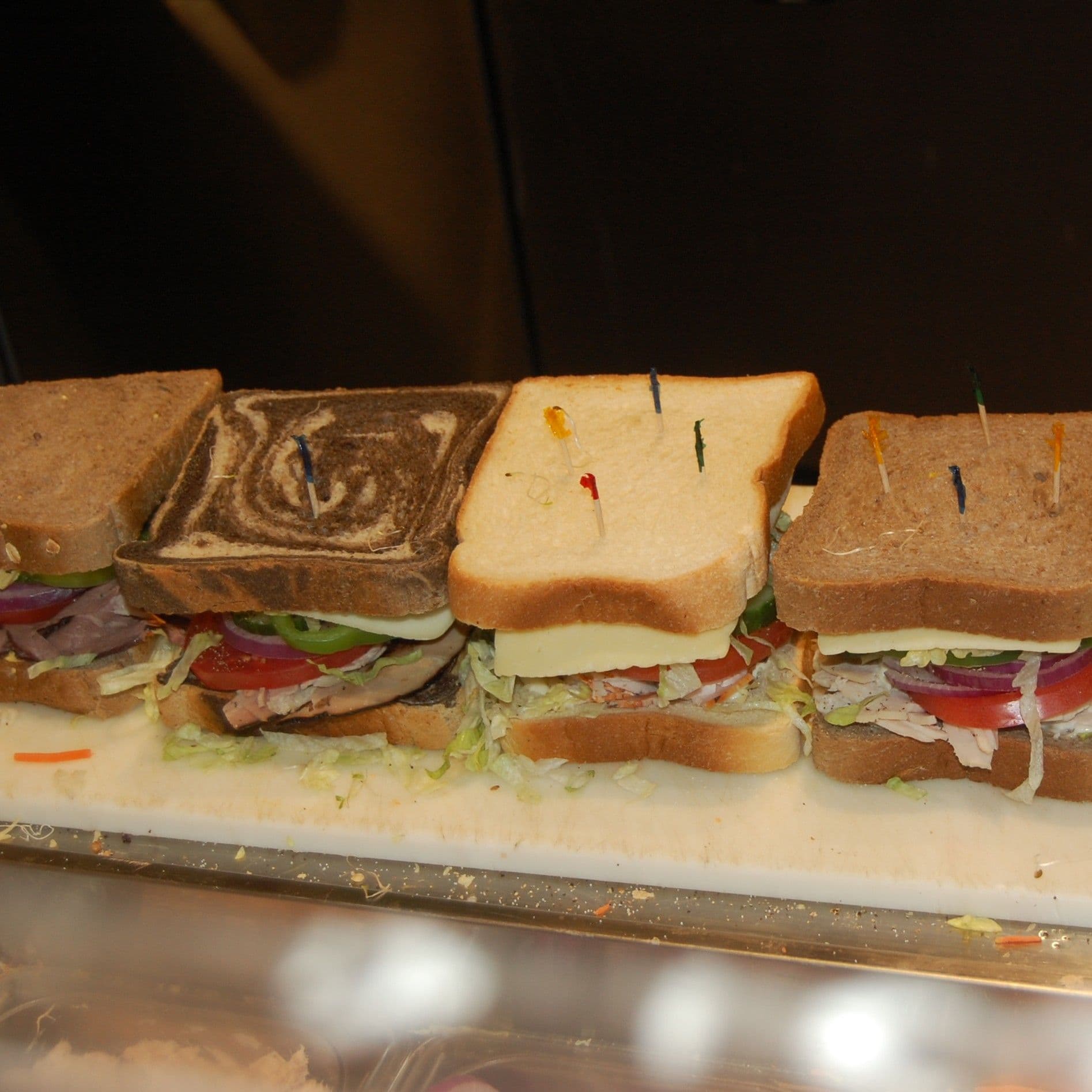 Row of stacked sandwiches in different breads on a deli board