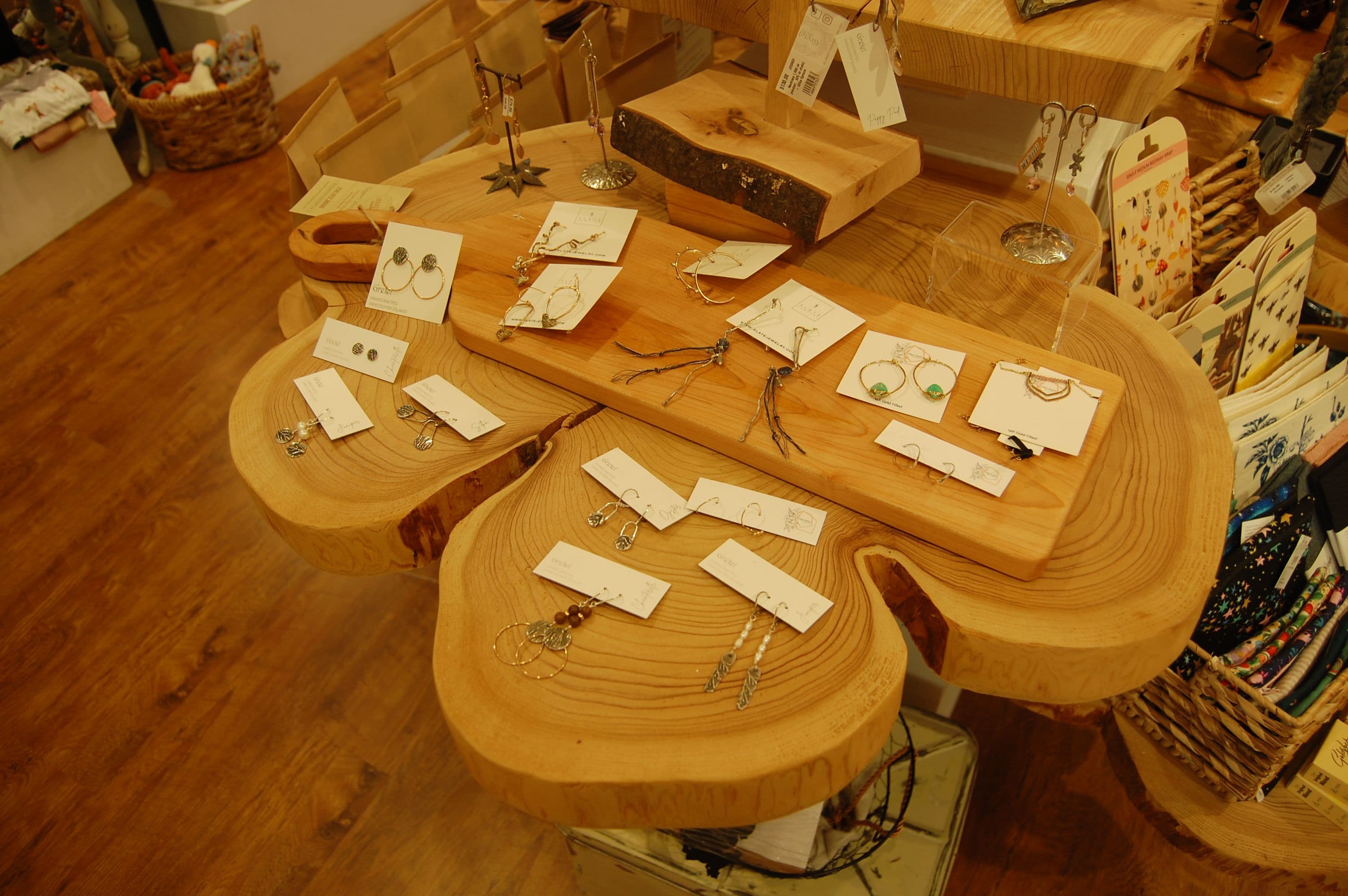 Top-down view of handmade earrings on cards across the wood-slab tables