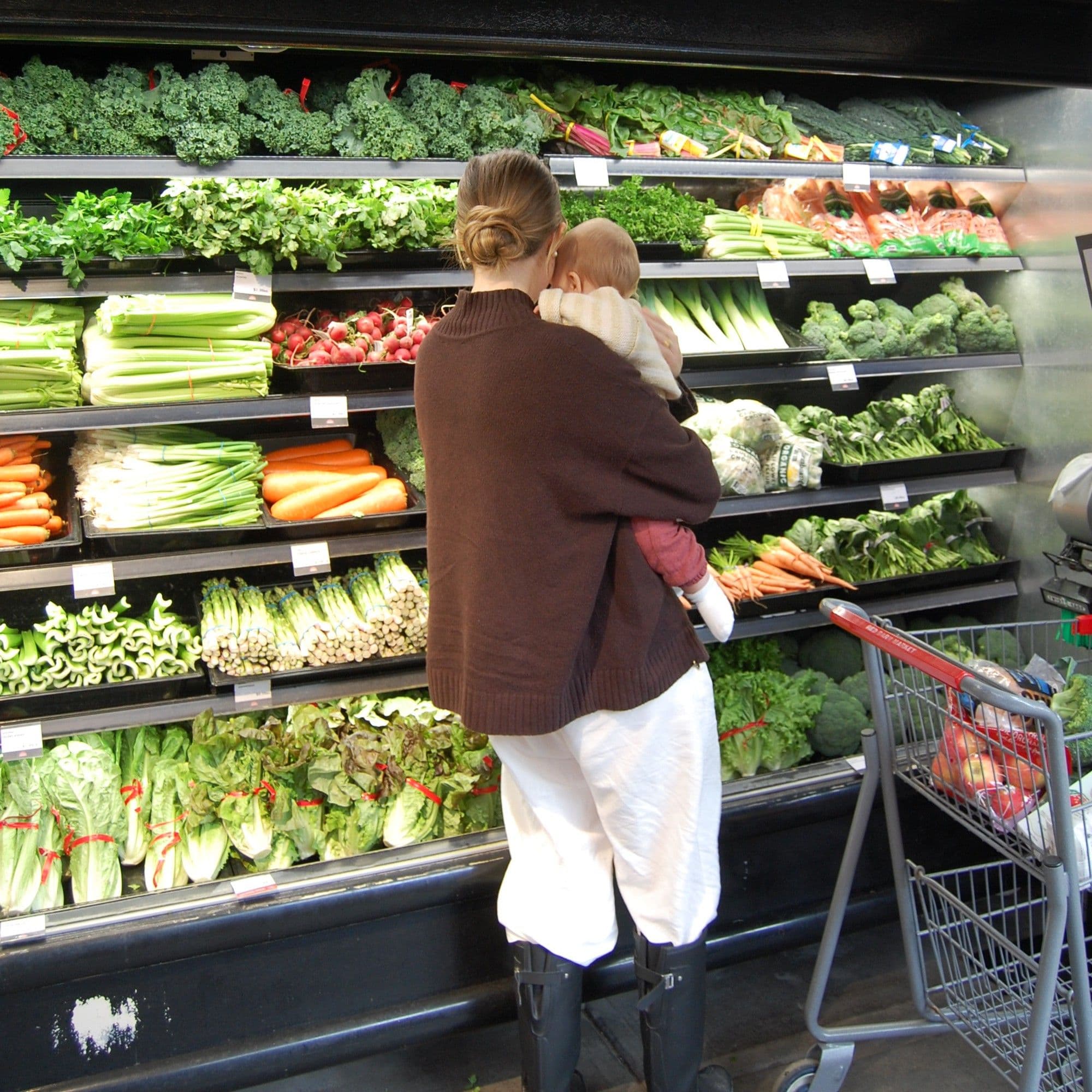 Mother holding her baby while shopping the vegetable display