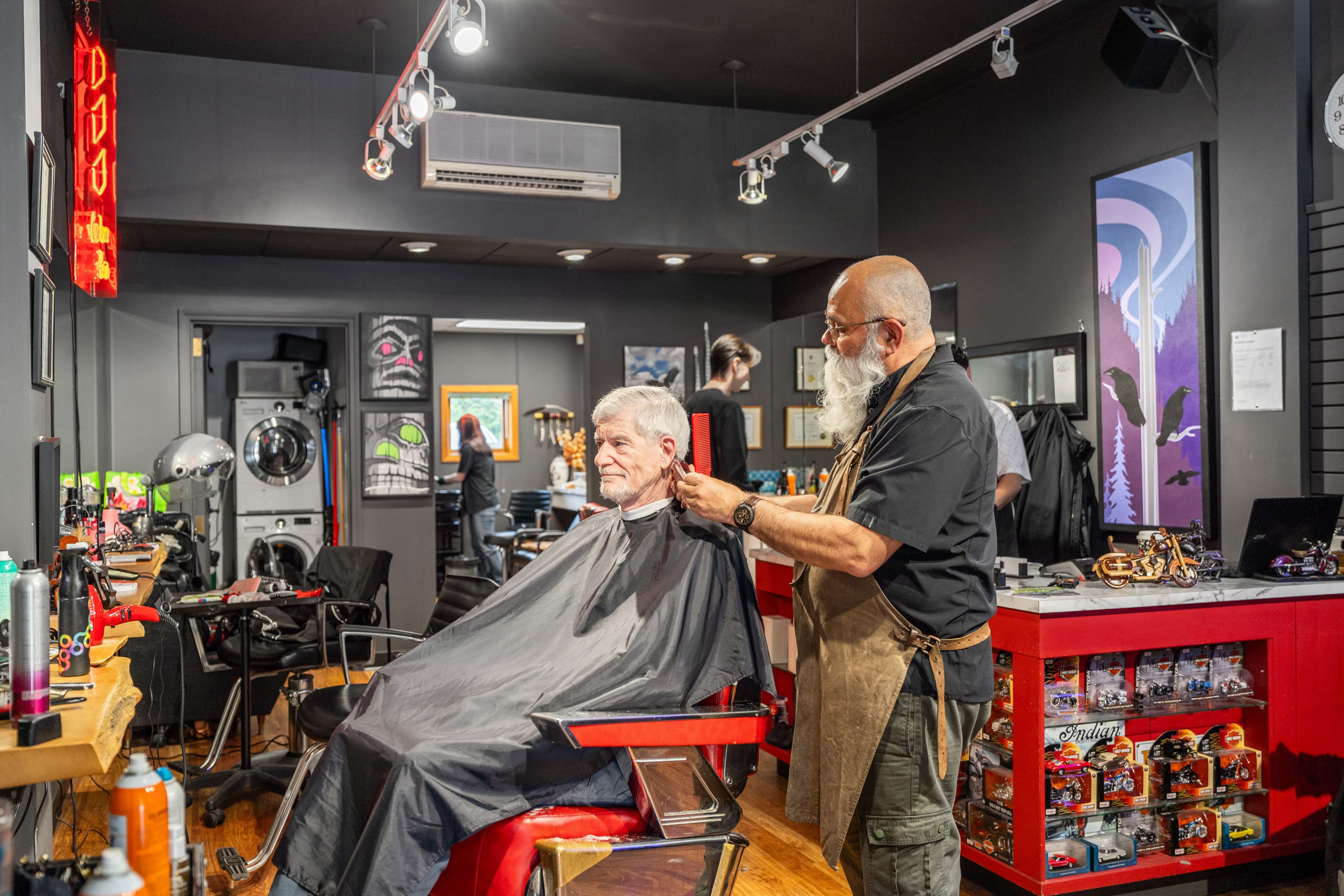 Barber giving an older customer a haircut in a vintage red chair, moody black-walled shop