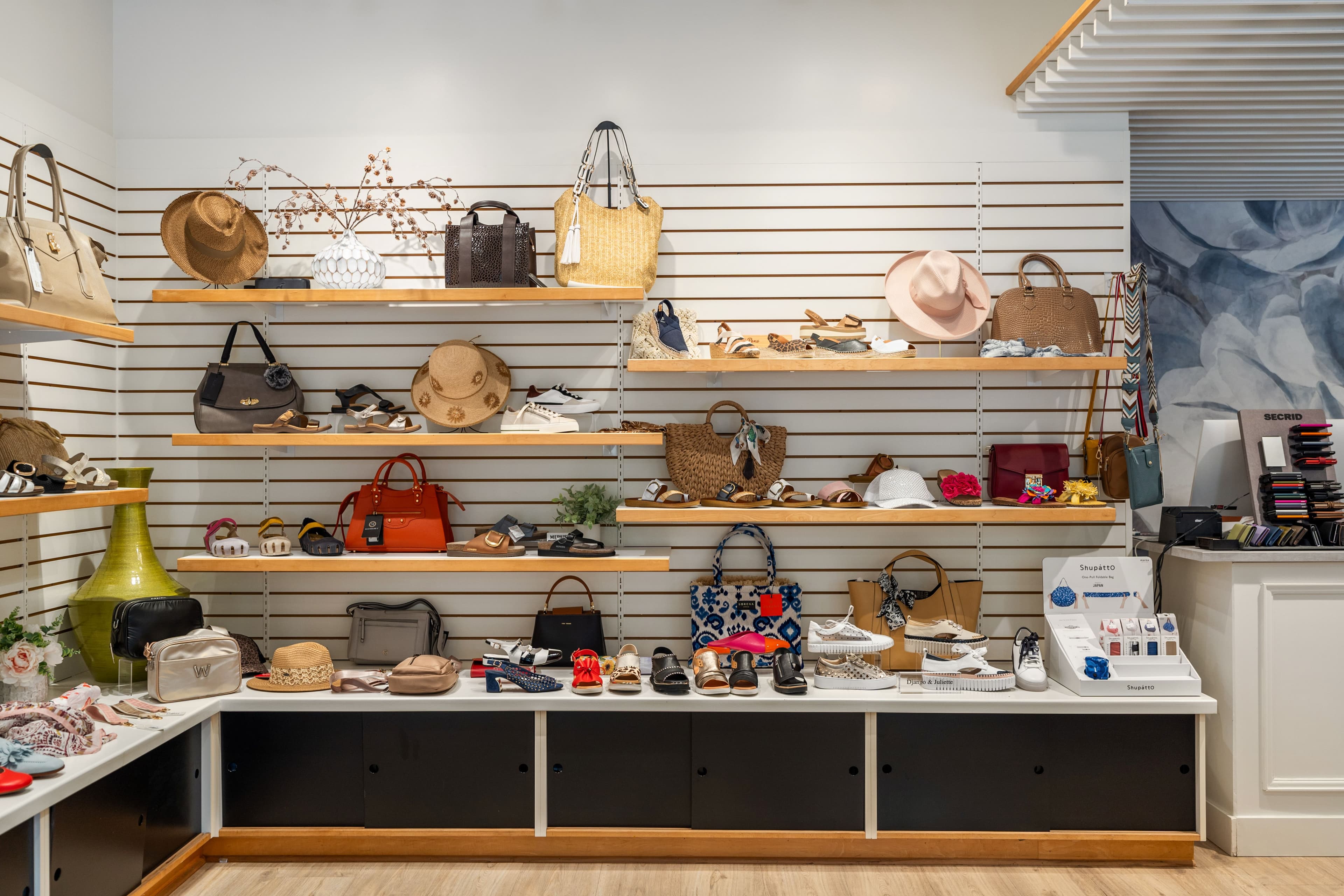 Wide retail wall with shelves of bags, hats and shoes on white slatwall