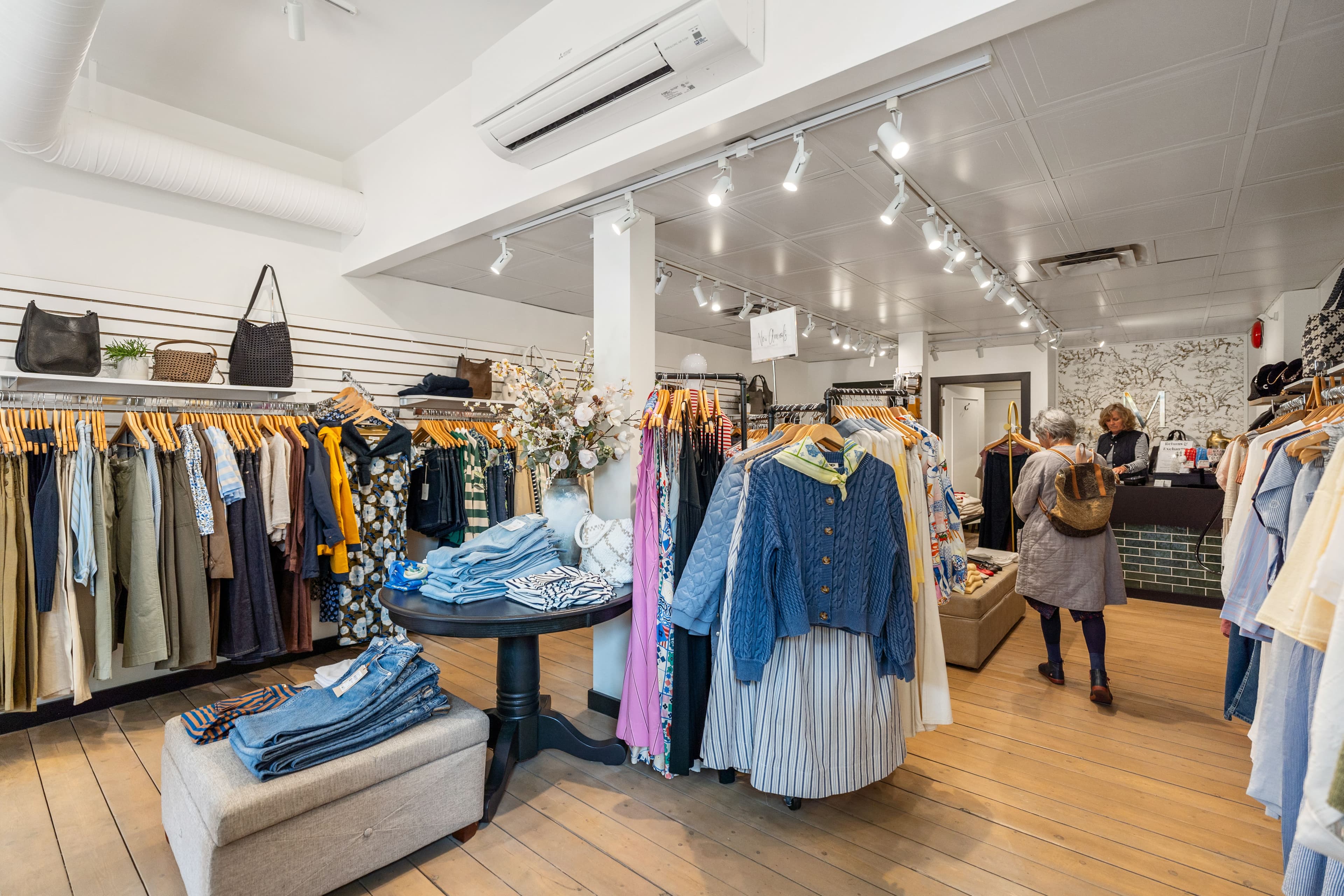 Moden Boutique interior with handbag wall, clothing racks and a denim-topped ottoman
