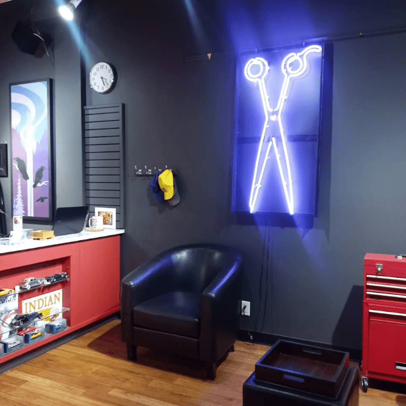 Lounge corner with leather chair and a glowing neon scissors sign