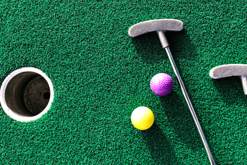Top-down view of a putter and colourful golf balls beside the hole