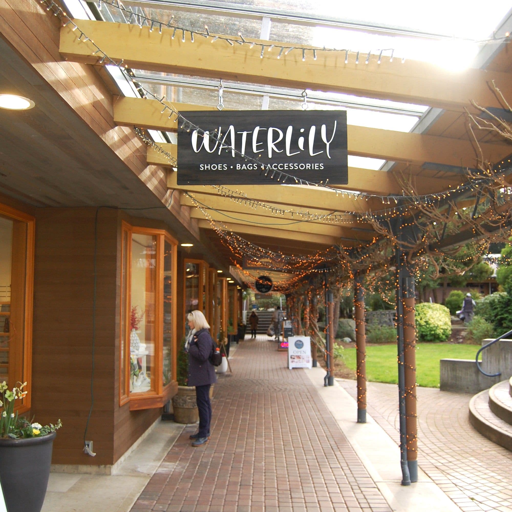 Waterlily Shoes • Bags • Accessories sign hanging beneath the courtyard walkway with twinkle lights