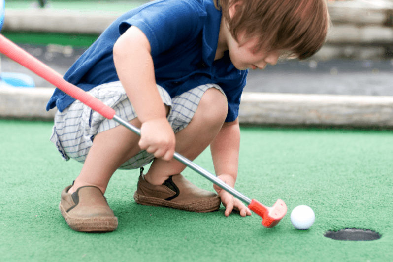 Child kneeling to line up a putt on the green course