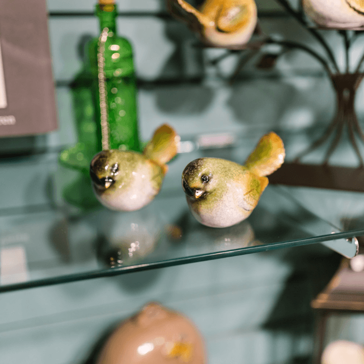 Pair of ceramic bird figurines on a glass shelf